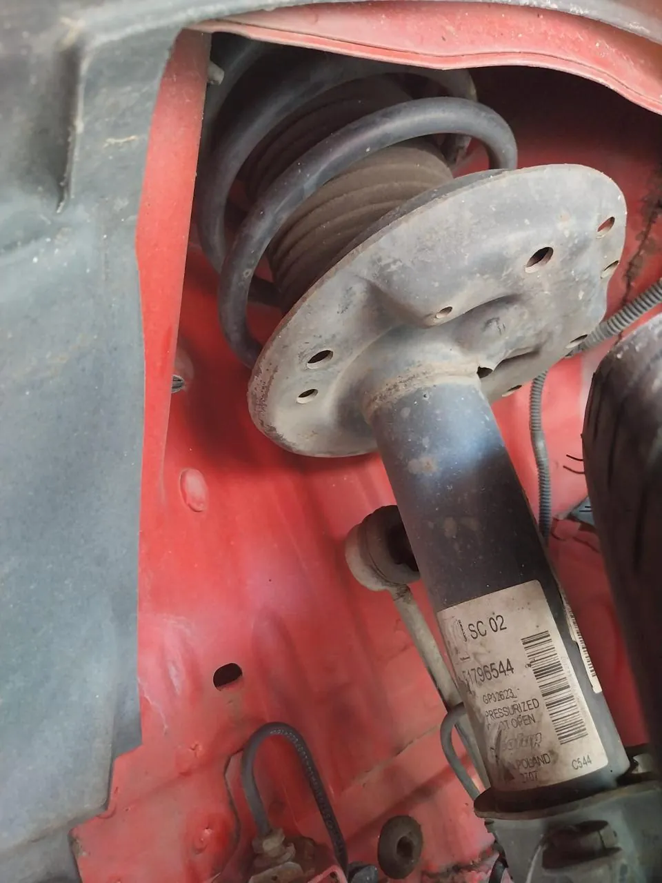 Amortiguador delantero con la etiqueta de fábrica, visto desde el paso de rueda de un coche rojo