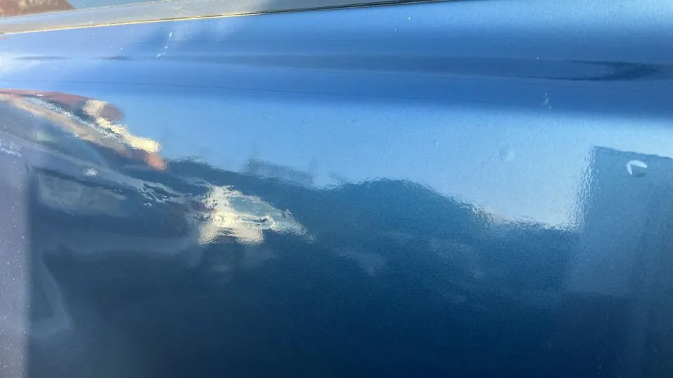 Reflejo ondulado sobre la pintura azul de un coche, señal de masilla bajo el repintado